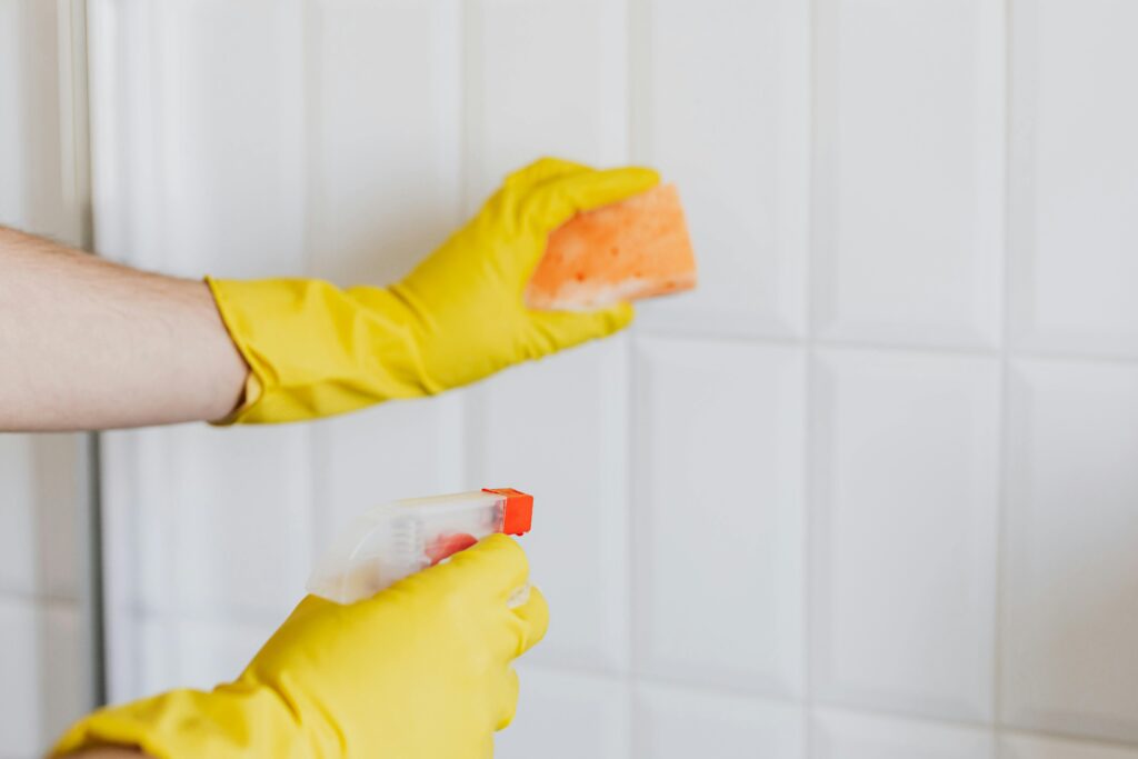 Professional cleaner sanitizing bathroom wall as part of thorough post tenancy cleaning service