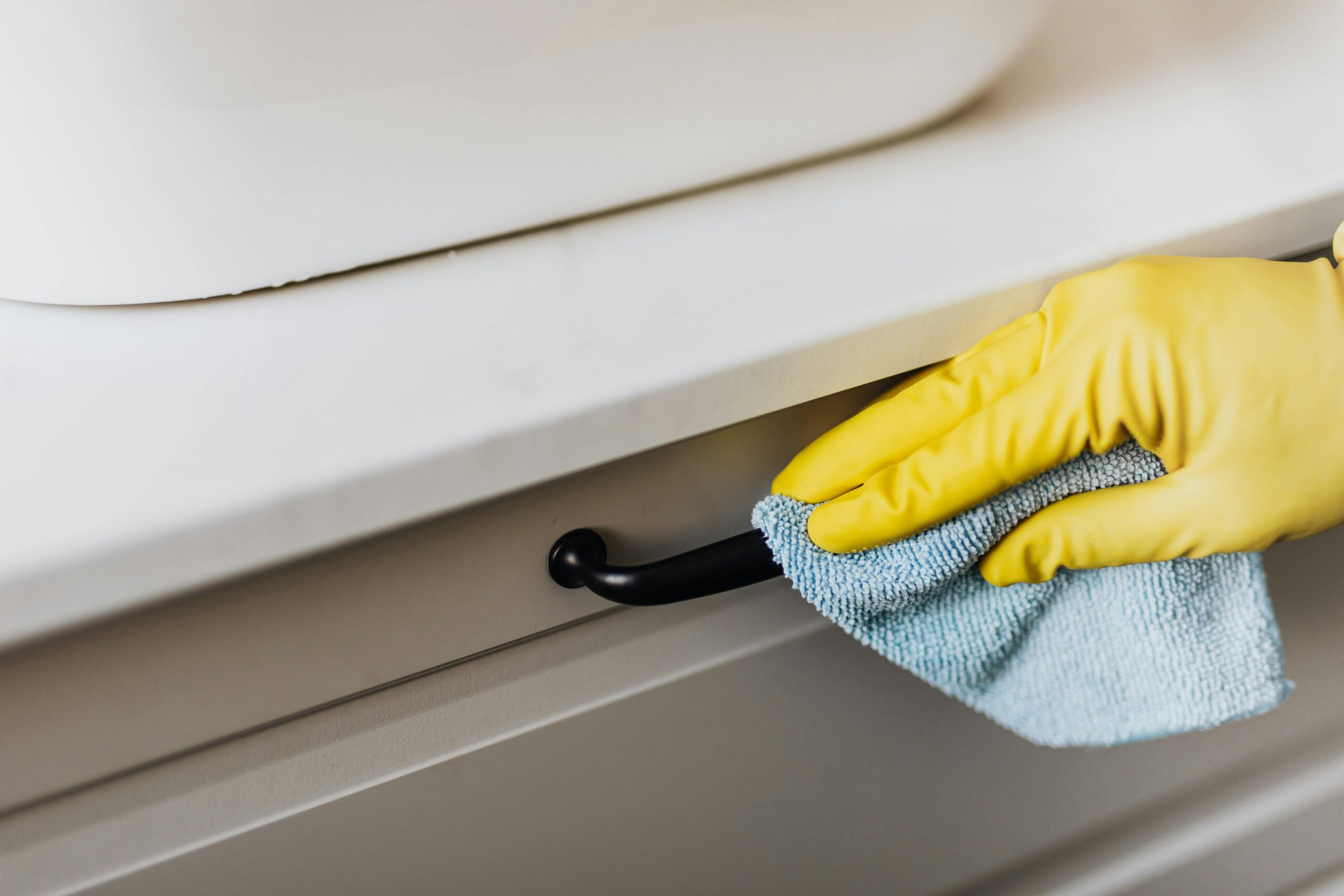 Professional cleaner wearing yellow gloves wiping a cabinet handle with a cloth