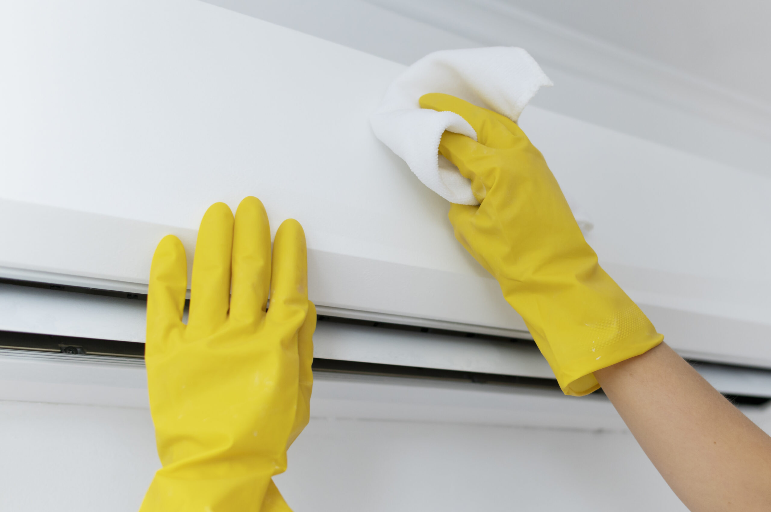 Hands in yellow gloves wiping and cleaning an air conditioner unit to improve indoor air quality.