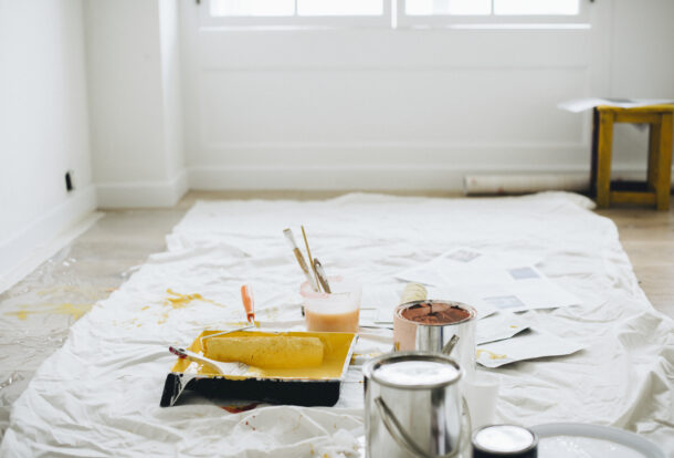 Paint cans, rollers, trays, and brushes scattered on a protective sheet in a bright room after renovation or painting work.